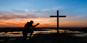 a man with the sunset behind him kneeling by a cross. ** Note: Visible grain at 100%, best at smaller sizes