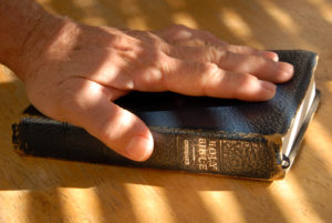 Hand On Well Used Old Bible Under Painted Light