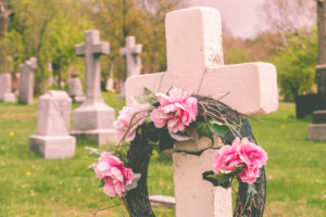 Funeral wreath with pink flower on a cross in a cemetary with a vintage filter.